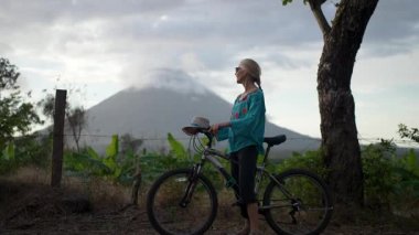 Son sınıf öğrencisi bir kadın Nikaragua 'daki Ometepe Adası' nda Concepcion volkanı yakınlarında bisiklet sürerken gülümsüyor. Etrafını saran yemyeşil bulutlar tepemizde toplanıyor..
