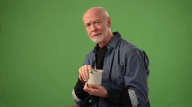 Son sınıf öğrencisi, üzgün bir ifadeyle elinde bir kupayla oturuyor. Katı yeşil arkaplan ürün yerleştirme veya duyurular için geniş bir alan sağlar.