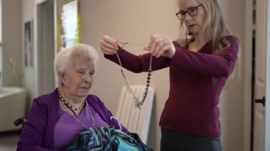 Bakıcı, yaşlı bir kadının giysilerini sıcak ve davetkar bir ev ortamında düzenlemesine yardımcı olur. Günlük aktiviteler sırasında şefkat ve destek gösterir..