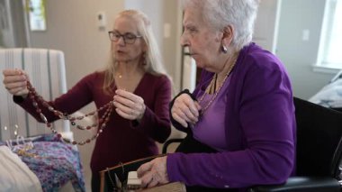 Olgun bir kadın, doğal ışıkla dolu sıcak ve davetkar bir mekanda takıları yaratıp takılara hayran olan yaşlı bir anneyle neşeli bir anı paylaşır..