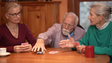 Aile üyeleri tahta bir masanın etrafında toplanıp iskambil oynuyor ve sıcak bir oturma odasında kahkahalarını paylaşıyorlar. Yaşlı çift kızlarıyla iyi vakit geçirmekten zevk alır..