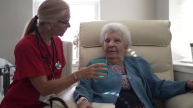 Bakıcı, yaşlı bir kadını rahat bir evde içki içmekten zevk alırken destekler, şefkat ve ihtiyarlarla olan bağlantısını vurgular..