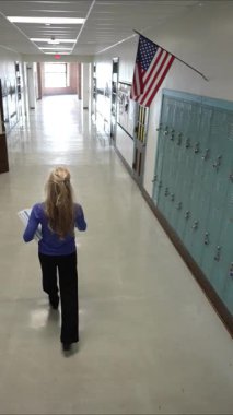 Yetişkin bir kadının günlük kıyafetlerle dolap dolu bir koridorda yürüdüğü dikey bir video. Yukarıda bir Amerikan bayrağı asılı, eğitici atmosferi geliştiriyor..