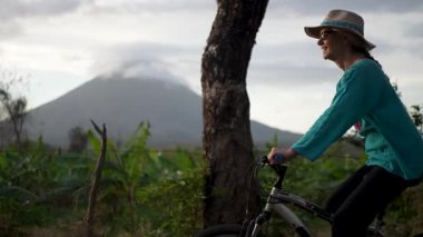 Gülümseyen son sınıf öğrencisi bir kadın Ometepe Adası 'nda bisikletiyle Nikaragua' daki Concepcion Volkanı 'nın keyfini sürüyor. Doğa onu bu güzel manzarayla çevreler..