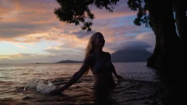 Mutlu, çekici, olgun bir kadın güneş batarken sakin sularda yürür. Etrafı güzel bir manzara ve Concepcion Volkanı 'nın siluetiyle çevrilidir..