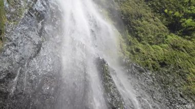 Kameralar, olgun yaşlı bir kadının Nikaragua, Ometepe 'deki çağlayan bir şelalenin altında, yemyeşil ormanlarla çevrili olduğunu gösteriyor. Güneş ışığı spreyde bir gökkuşağı yaratır..