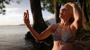 Neşeli, olgun bir kadın, güneş Concepcion Volkanı 'nın arkasında batarken gölün kenarında fotoğraf makinesiyle poz veriyor ve Nikaragua' da neşeli bir anı yakalıyor..