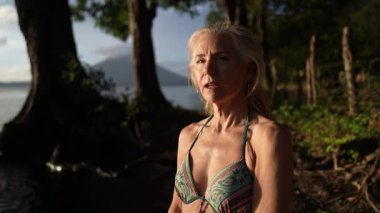 Olgun bir kadın Nikaragua 'da sakin bir gölün yanında duruyor. Güneş Concepcion yanardağının arkasında huzur içinde batarken gülümsüyor. Elleri kalbin üzerinde, kendine sarılıyor..