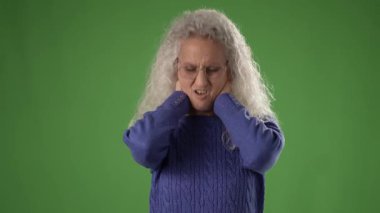 50 'li yaşlarda, kıvırcık gri saçlı, gözlüklü, mavi kazaklı, canlı yeşil bir ekranın karşısında gülümseyen olgun bir kadın..