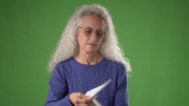 50 'li yaşlarda, uzun, dalgalı gri saçlı olgun bir kadın memnuniyetle mektup okur. Gözlük takıyor ve gösteriş yapıyor. Sıcak bir gülümseme, anın tadını çıkarıyor..