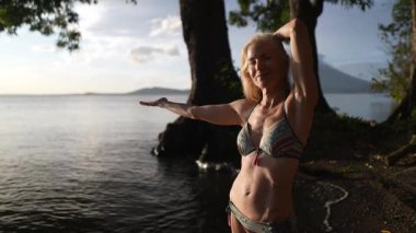 Çekici, mutlu, olgun bir kadının portresi Nikaragua 'da bir gölde bikini giyer ve Concepcion volkanı tarafından tatili boyunca sıcak gün batımını ve doğal güzelliği kucaklar..