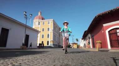Olgun bir kadın, Nikaragua, Granada 'da renkli bir katedralin önünde bisikletini sürerken geniş bir gülümseme sergiliyor. Onun neşeli deneyimi Orta Amerika 'nın özünü yansıtıyor..