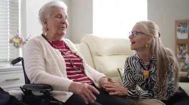 Columbia, MD, ABD - 12252024: 90 'lı yaşlarda yaşlı bir kadın, sıcak bir oturma odasında kızıyla samimi bir kahkaha paylaşıyor, aile ziyareti sırasında sevgi gösteriyor.