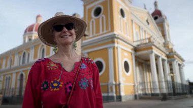 Olgun bir kadın, güneşli bir günde, renkli bir kıyafet ve güneş şapkası giyerek, Nikaragua, Granada 'nın canlı sokaklarını keşfederken ışıl ışıl gülümser..