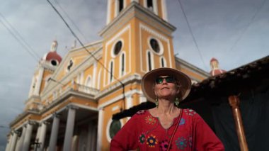 Olgun bir kadın, Nikaragua, Granada 'da canlı bir kilisenin önünde durup Orta Amerika macerası sırasında neşesini gösterirken başparmağını kaldırıyor..