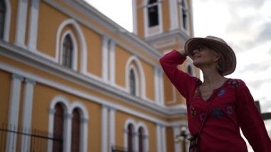 Olgun bir kadın, güneşli bir öğleden sonra Granada, Nikaragua 'nın renkli mimarisini keşfederken parlak giysiler içinde gülümseyerek yerel kültürü kucaklıyor..