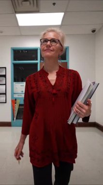 Dikey video geniş açı yavaş çekim görüntüsü mutlu olgun kadın öğretmen yürüyor ve boş okul koridoru.