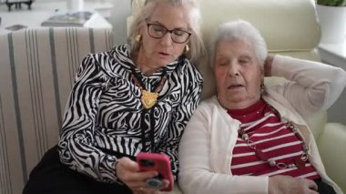 Yaşlı bir anne, evinde rahat rahat otururken gülümseme ve kahkahaları paylaşan kızıyla video görüşmesinden zevk alır..