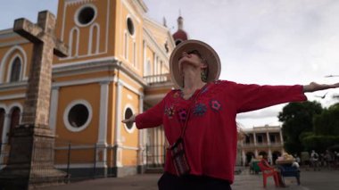 Olgun bir kadın, Granada, Nikaragua 'daki canlı atmosferi kucaklıyor. Kollarını renkli koloni mimarisinin arka planına mutlulukla açıyor..