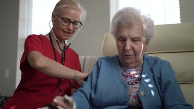 Bakıcı, yaşlı bir kadına sıcak bir şekilde bakar, bir sağlık merkezinde destek ve arkadaşlık sağlar. Onların etkileşimi rahatlığı ve refahı teşvik eder..