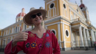 Neşeli bir ifadeye sahip bir turist, Granada, Nikaragua 'nın tarihi sarı mimarisinin önünde poz vererek benzersiz tarzını ve heyecanını sergiliyor..