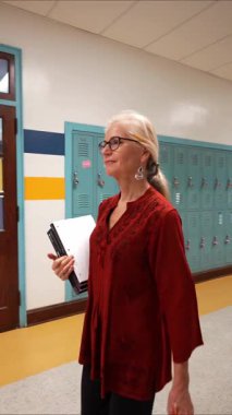 Berkeley Springs, WV, ABD - 12 23 2021: Dikey video kamera, Amerikan bayrağıyla boş okul koridorunda yürüyen bir yavaş çekim öğretmenini izliyor.