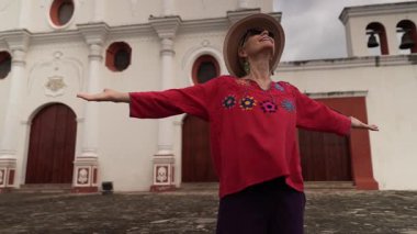 Olgun bir kadın, Granada, Nikaragua 'daki bir manastır katedralinin önünde kollarını açmış, hareketli yerel kültürü tecrübe ederek anı kucaklıyor..