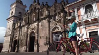 Gülümseyen bir kadın, bisikletiyle poz veriyor. Granada, Nikaragua 'daki tarihi La Merced Kilisesi' nin önünde telefon ediyor. Keyifli bir seyahat anı yakalıyor..