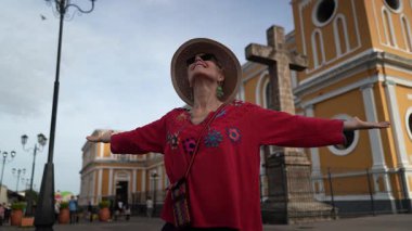 Granada Katedrali, Nikaragua 'nın güzelliğini kucaklayan kolları açık bir kadın, tarihi mimarinin yanında güneşli bir günün tadını çıkarırken renkli bir bluz ve şapka giyiyor..