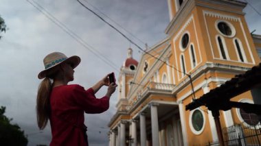 Hasır şapkalı olgun bir kadın, Granada, Nikaragua 'daki renkli mimarinin dramatik bir gökyüzü altında yerel kültürü kucaklayan fotoğraflarını çekiyor..