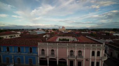 Granada, Nikaragua, uzaktaki tarihi bir kilisenin çarpıcı mimarisi tarafından çerçevelenmiş renkli bir günbatımının altında canlı çatılar sergiliyor..