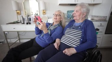 Yaşlı bir kadın tekerlekli sandalyede otururken kızıyla görüntülü sohbet etmekten hoşlanıyor. Birlikte gülümsüyorlar, sıcacık bir evde anılara değer veriyorlar..