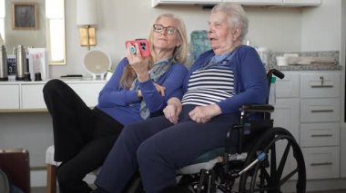 Tekerlekli sandalyedeki yaşlı bir kadın kızıyla görüntülü sohbetten hoşlanıyor. Sevgi ve destek dolu sıcak bir evde anılarını ve kahkahalarını paylaşıyor..