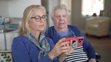 Kapalı bir ortamda, bir kadın yaşlı annesine tekerlekli sandalyede destek olur. Yürekten bir ziyaret sırasında akıllı telefondan anılarını paylaşırlar..