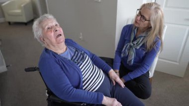 Ev ortamında, 90 'lı yaşlarda bir kadın tekerlekli sandalyede otururken, kızı aile ziyareti sırasında arkadaşlık, ilgi ve sevgi sunuyor..