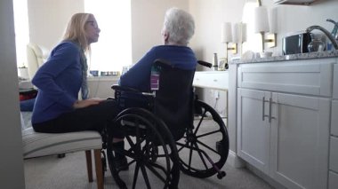 Bir kadın sandalyeye oturur ve yaşlı annesiyle evde tekerlekli sandalyede samimi bir konuşma yapar. Onların bağları günlük hayatta sevgi ve ilgiyi yansıtır..