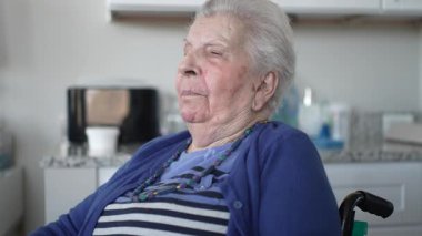 90 'lı yaşlarda, tekerlekli sandalyede oturan, sıcak bir ev ortamında ailesiyle samimi bir ziyaret yapan, sevgisini ve desteğini paylaşan yaşlı bir kadın..