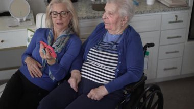 Tekerlekli sandalyedeki yaşlı bir kadın kızıyla görüntülü sohbetten zevk alıyor. Evlerinde samimi bir ziyaret sırasında sevgi ve hatıralar besliyor..
