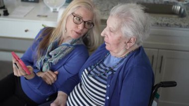 Bir kız, evde rahat bir ortamda yaşlı annesiyle iletişim kurar, fotoğraflara bakmak ve hatıralarını paylaşmak için akıllı bir telefon kullanır, birlikte geçirdikleri güzel anları ön plana çıkarır..