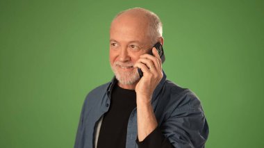 Sakallı olgun bir adam, yeşil arka planda telefonla konuşurken gülümsüyor. Duygularını dile getiriyor ve önemli bir duyuru yapıyor..