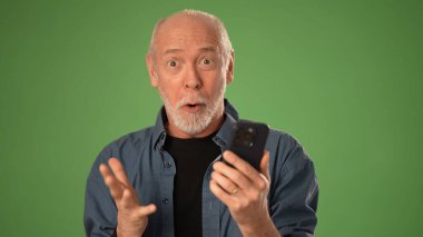 Olgun bir adam, elinde akıllı bir telefonla sevinçle tepki verirken heyecan gösterir. Katı yeşil arka plan onun anlamlı portresine odaklanıyor..