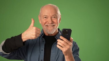 Olgun bir adam akıllı bir telefonu tutarken gülümser, yeşil arka plana karşı olumlu bir hareket ile olumlu ifade eder. Ürün duyuruları için mükemmel.