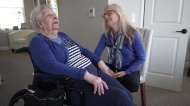 90 'lı yaşlarda bir kadın evinde tekerlekli sandalyede otururken, kızı onunla özen ve sevgiyle konuşuyor, yakın bağlarını ve günlük yaşamlarını vurguluyor..