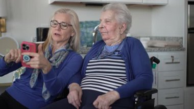 Tekerlekli sandalyedeki yaşlı bir kadın kızıyla görüntülü sohbet etmekten hoşlanıyor. Hem gülümsüyor hem de rahat evlerinde anılarını paylaşıyor..
