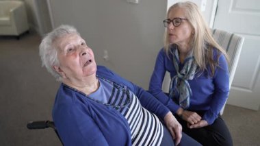 90 'lı yaşlarda yaşlı bir kadın sevgi dolu sıcak bir aile ziyareti sırasında evinde tekerlekli sandalyede oturuyor ve kızından ilgi görüyor..