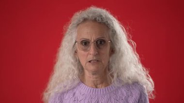 Beyaz saçlı ve gözlüklü orta yaşlı bir kadın yoğun bir öfke ve mutsuzluk sergiliyor..