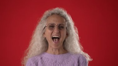 Lavanta süveter giyen mutlu orta yaşlı bir kadın gülüyor, eğlencesini canlı bir ortamda, çarpıcı kırmızı bir arka planda sergiliyor..