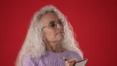 Beyaz saçlı ve gözlüklü orta yaşlı bir kadın derin düşüncelere dalmış elinde bir kalem ve defterle günlüğe yazıyor. Onun canlı süveteri çarpıcı kırmızı arka planla çelişiyor.