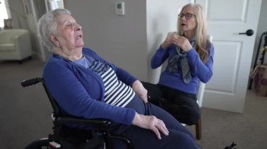 Kapalı bir ortamda, 90 'lı yaşlarda yaşlı bir kadın tekerlekli sandalyede oturuyor. Kızı ziyaret sırasında sevgi ve destek sağlıyor, bağlarını vurguluyor..