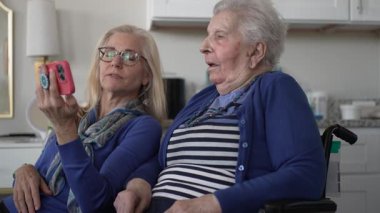 Tekerlekli sandalyedeki yaşlı bir kadın kızıyla görüntülü konuşma yapar, sıcak bir ev ortamında neşeli anılar yakalar..